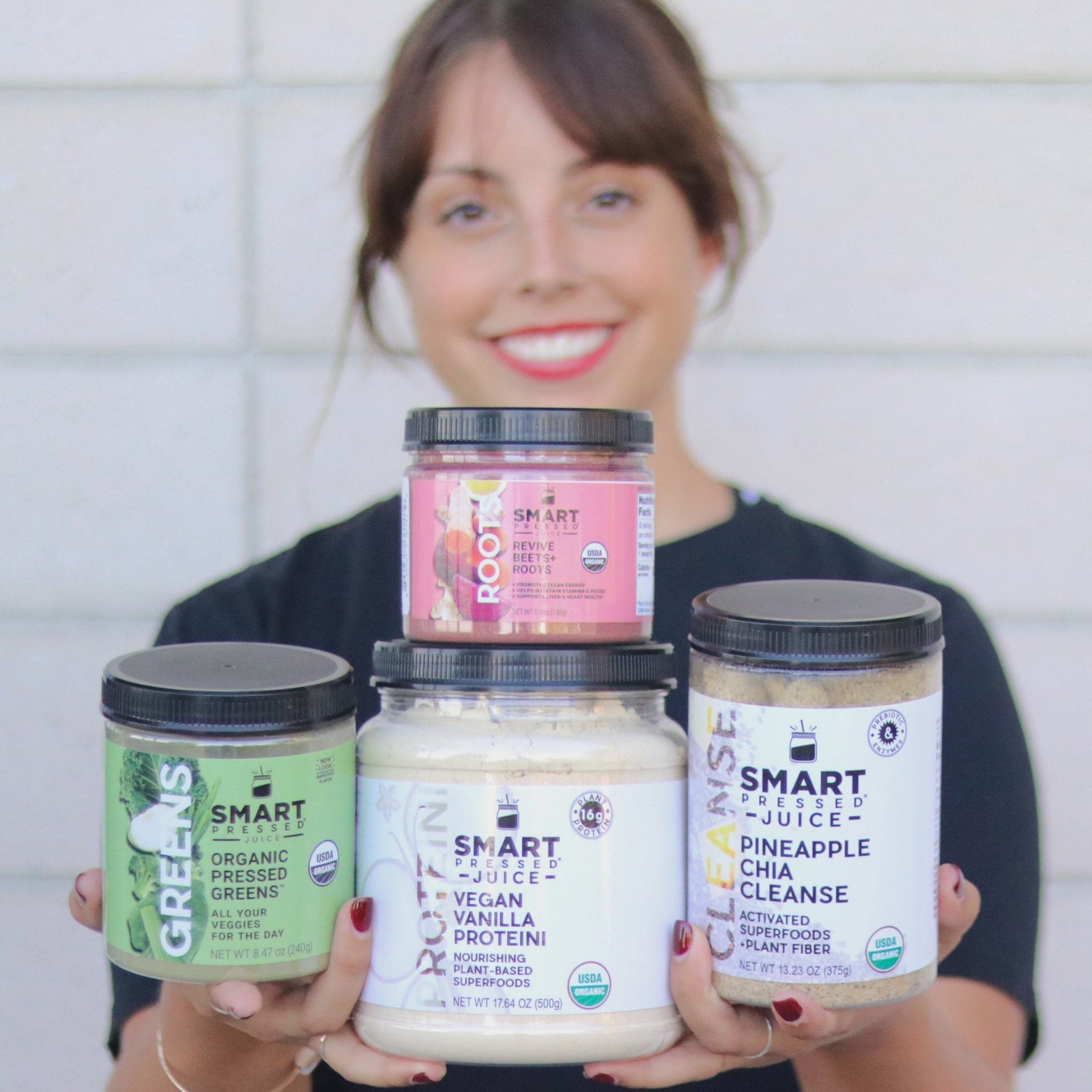Image of a white background and a woman holding 4 protein shakes on her hand