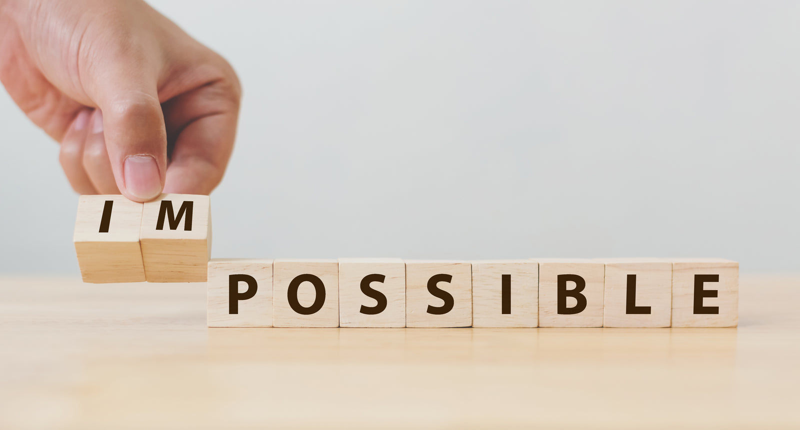 Blocks letters spelling out impossibe with hand removing the letters IM to spell "POSSIBLE"