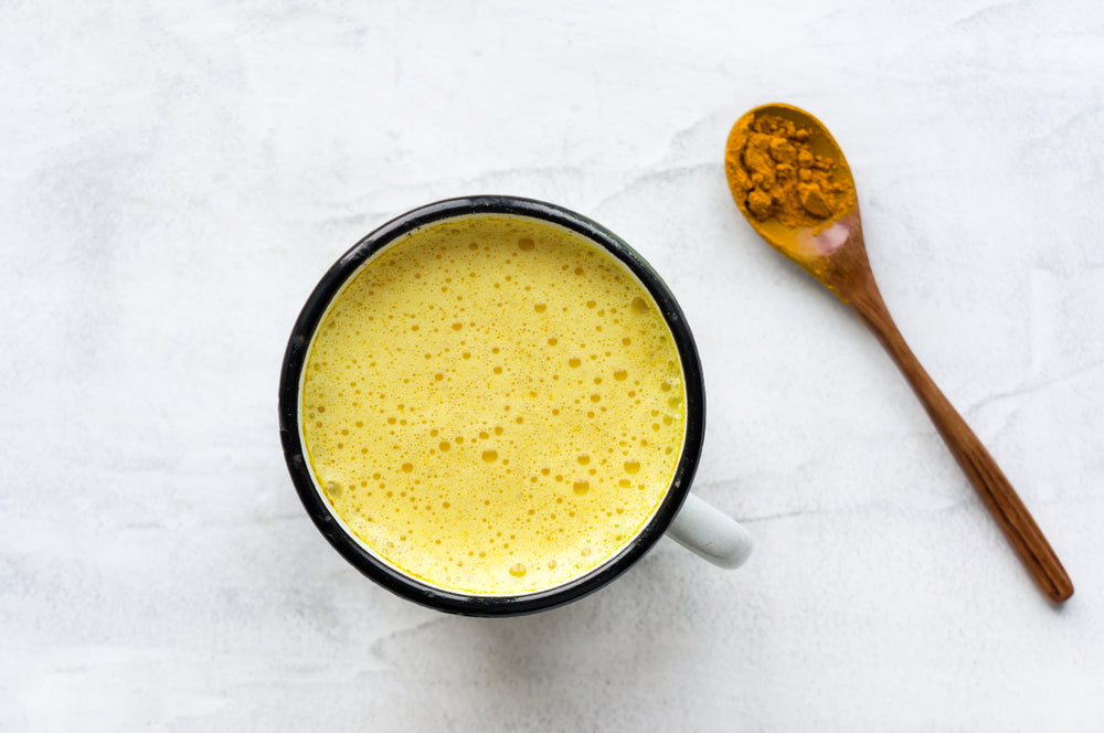 a top view of a cup on a white background filled with golden milk pineapple chia and a wooden spoon full of turmeric powder 
