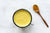 a top view of a cup on a white background filled with golden milk pineapple chia and a wooden spoon full of turmeric powder 