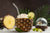 A serve of Pineapple Whip Debloating Smoothie inside a pineapple, next to a disco ball and pineapple